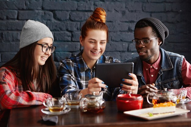 Internationale Gruppe von drei Freunden, die im Café sitzen und Videos online mit Tablet ansehen