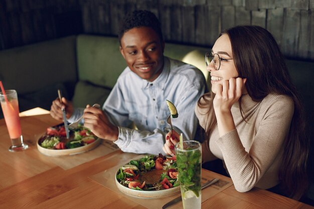 Internationale Leute sitzen am Tisch mit Salaten und Cocktails