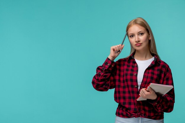 Internationaler Studententag junges süßes Mädchen in rot kariertem Hemd, das mit Bleistift und Notizbuch denkt