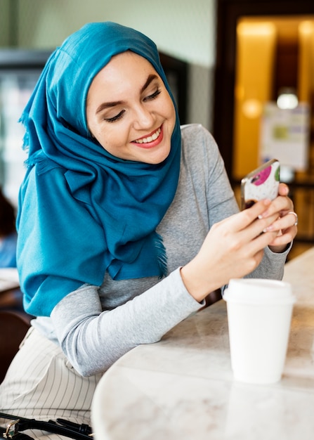 Islamische Frau, die intelligentes Telefon und das Lächeln verwendet