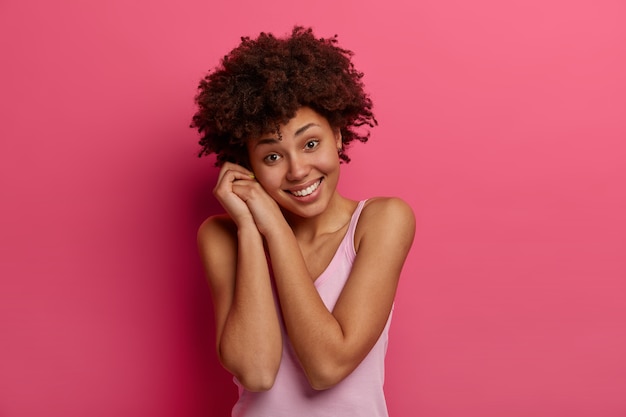 Isolierte Aufnahme der hübschen gesunden Frau lächelt sanft, neigt den Kopf und genießt angenehmes Gespräch, lässig gekleidet, freudig, Modelle gegen rosa Wand. Positives Emotionskonzept