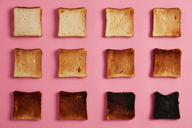 Isolierte Überkopfaufnahme von Brottoast in verschiedenen Stadien des Röstens vor rosigem Hintergrund. Die letzte Scheibe ist vollständig verbrannt. Snack zum Frühstück. Von ungeröstet bis verkohlt. Lebensmittelfotografie