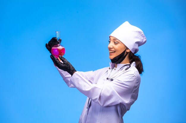 Isolierte krankenschwester in hand und gesichtsmaske zeigt flasche mit rosa flüssigkeit und lächelt.