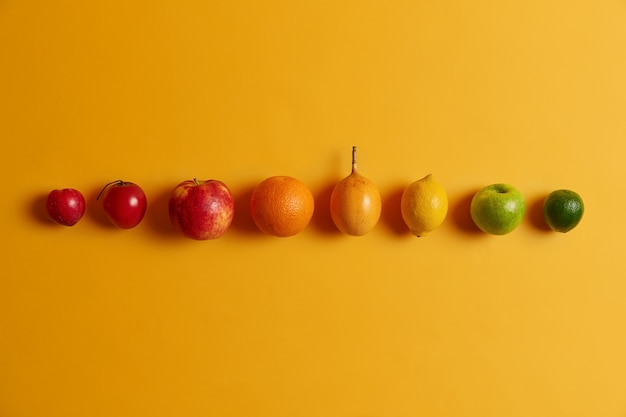 Isolierte Zitrusfrucht in Reihe gegen gelben Hintergrund. Grüne Limette, Apfel, Zitrone, Cumquat, Orange, Fortunella und Pfirsich. Nahrhafte tropische Früchte, die eine Vielzahl von Vitaminen enthalten, um Sie gesund zu halten