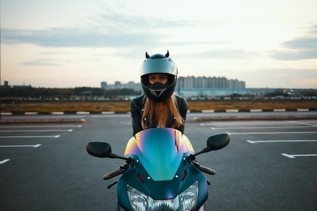 Isoliertes Bild des blonden weiblichen Rennfahrers in der speziellen Schutzausrüstung, die auf blauem Motorrad sitzt. Extrem, Geschwindigkeit, Adrenalin und moderner aktiver Lebensstil