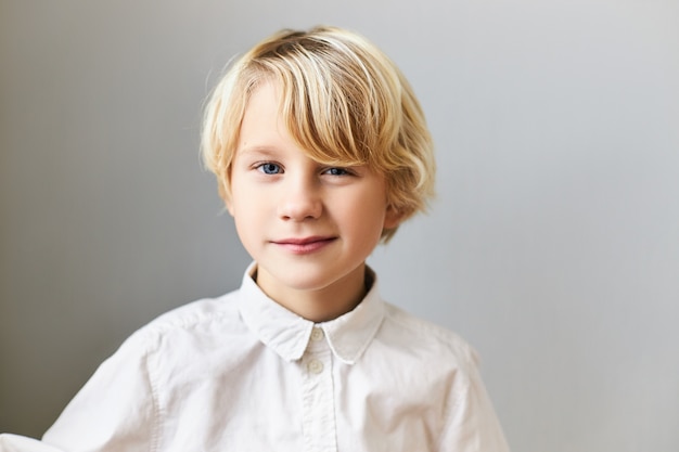 Isoliertes Bild des emotionalen fröhlichen blauäugigen kaukasischen Jungen mit hellem Haar, das spielerischen Gesichtsausdruck hat. Kinder, Spontanität, glückliche Kindheit und positive Emotionen