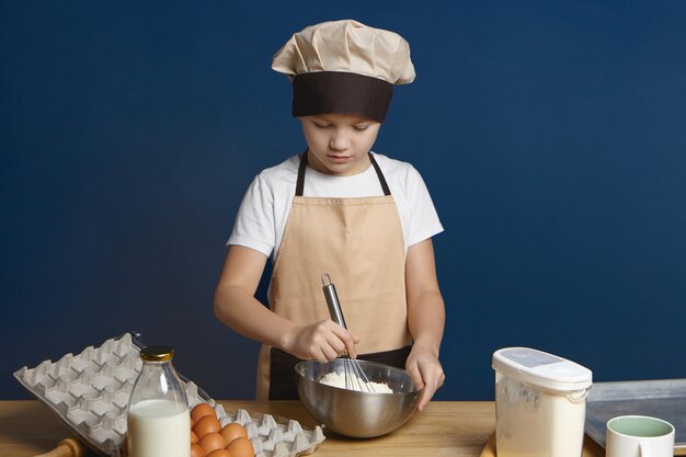 Isoliertes Porträt des niedlichen Teenagers, der lernt, wie man Kekse am kulinarischen Workshop macht