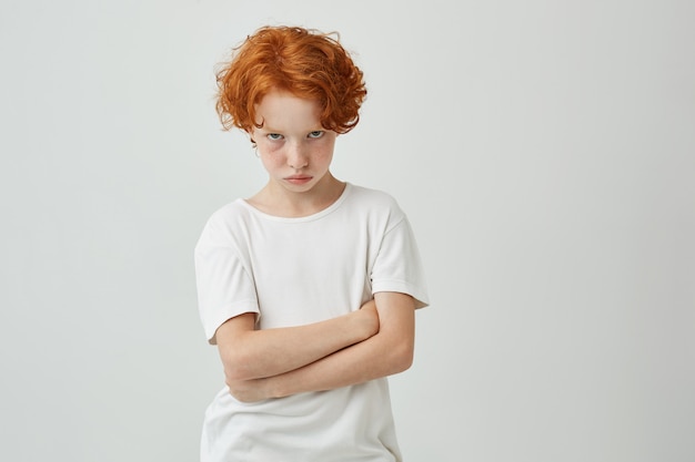 Isoliertes Porträt des unglücklichen kleinen Kindes mit den roten gelockten Haaren und den Sommersprossen, die beleidigt werden