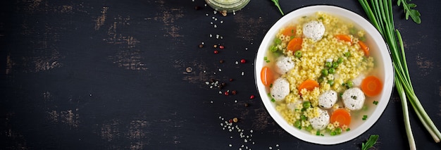 Italienische Fleischbällchensuppe und glutenfreie Nudeln von Stelline in der Schüssel auf schwarzem Tisch.