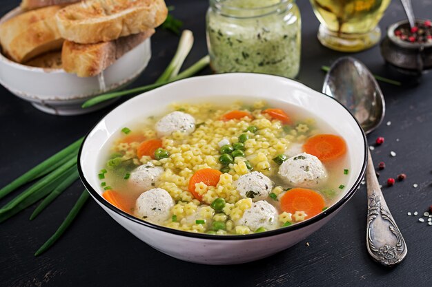 Italienische Fleischbällchensuppe und glutenfreie Nudeln von Stelline in der Schüssel auf schwarzem Tisch.