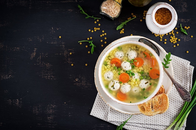 Italienische Fleischklöschensuppe und stelline Teigwaren in der Schüssel auf schwarzer Tabelle.