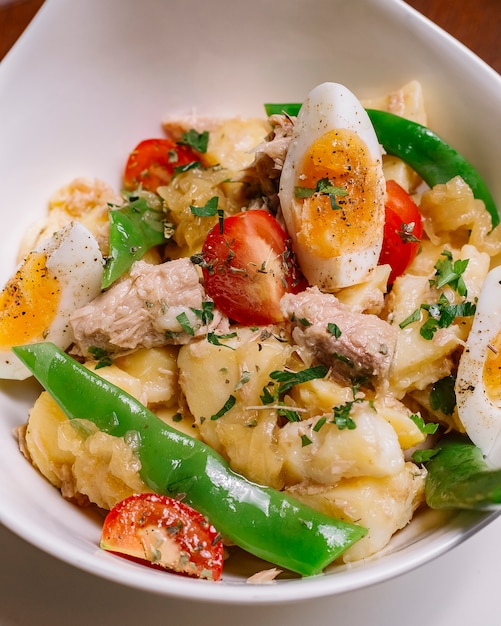 Italienische Kartoffelsalatschale mit Thunfischbohnen-Kirschtomaten-Petersilie gekochten Eiern und Olivenöl vertikal