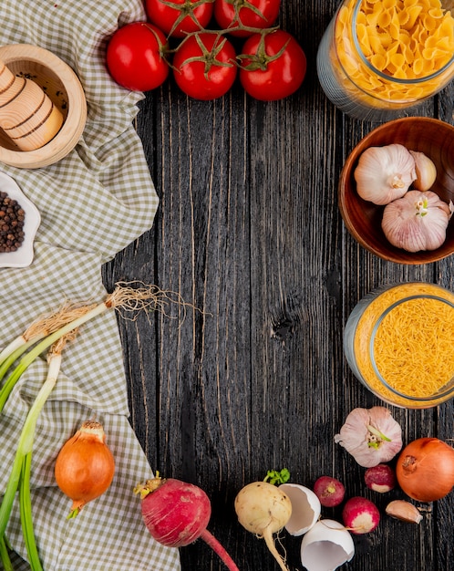 Italienische Pasta Farfallini Fellini Knoblauch Tomaten Mörser Pfeffer Zwiebel auf dem hölzernen Hintergrund oben vie Kopie Raum