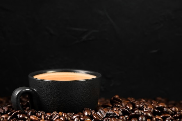 Italienischer Espresso in einer schwarzen Tasse Kaffee zum Frühstück Tasse frischen Kaffee unter Kaffeebohnen Nahaufnahme