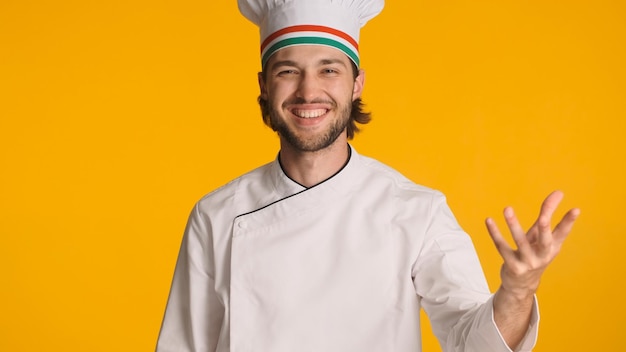 Kostenloses Foto italienischer küchenchef gekleidet in uniform suchen glücklich lächelnd in die kamera über farbigen hintergrund mann in kochmütze posiert im studio