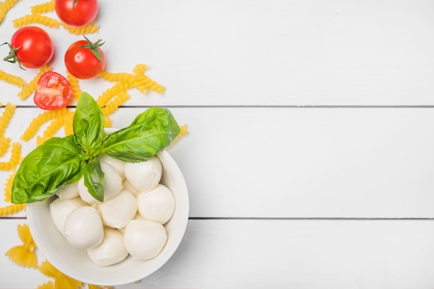 Italienischer Mozzarella-Käse mit Basilikumblatt; Tomaten und Fusilli-Nudeln auf weißem Holzbrett