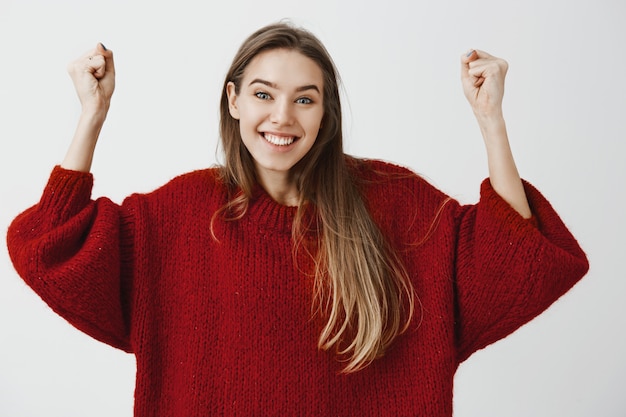 Ja, wir haben es geschafft, lasst uns anfangen zu feiern. porträt einer positiv optimistischen, gut aussehenden studentin in einem losen pullover, die triumphierend die arme hebt, einen freund aufheitert, der den ersten preis gewonnen hat, und breit lächelt