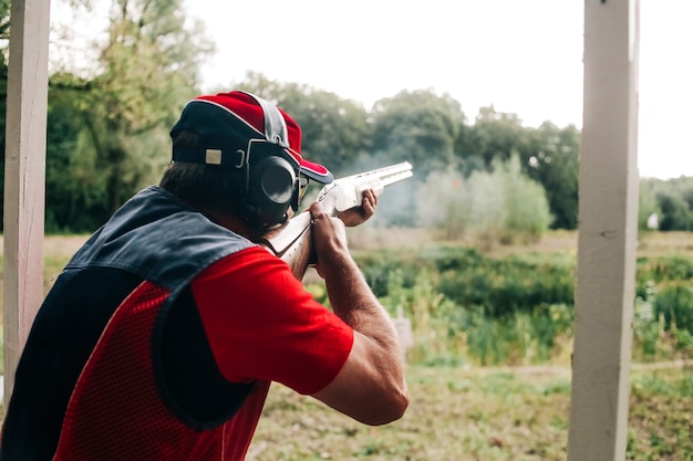 Jäger schießt mit einer Schrotflinte auf ein Ziel in speziellen Klamotten und Kopfhörern