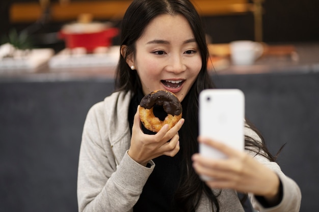 Japanische Frau macht Selfie, während sie einen Donut isst