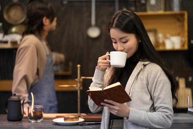 Japanische Frau trinkt Kaffee und liest aus einem Notizbuch in einem Restaurant