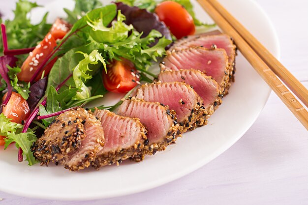 Japanischer traditioneller Salat mit Stücken von mittel-seltenem gegrilltem Ahi-Thunfisch und Sesam mit frischem Gemüsesalat auf einem Teller.