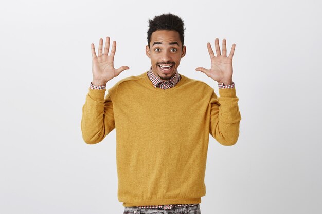 Jazzhände immer im Trend. Porträt eines glücklichen emotionalen jungen Mannes mit Afro-Haarschnitt, der Palmen hebt und breit lächelt, sich ergibt und Freundlichkeit und gute Laune ausdrückt