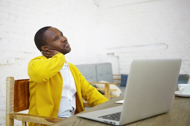 Job, Kreativität, Beruf und freiberufliches Konzept. Porträt des stilvollen wohlhabenden dunkelhäutigen männlichen Unternehmers, der vor offenem Laptop am Schreibtisch sitzt und an Startprojekt arbeitet, das nachdenklichen Blick hat