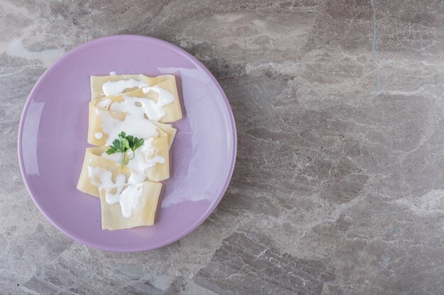 Joghurt auf Lasagneblättern mit Grüns auf dem Teller, auf der Marmoroberfläche.