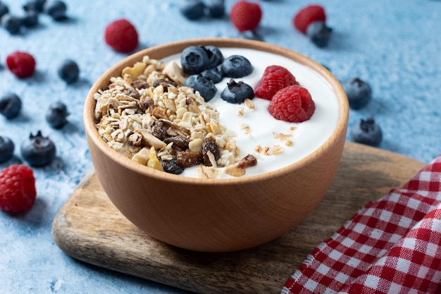 Joghurt mit Beeren und Müsli zum Frühstück in Schüssel auf blauem Hintergrund