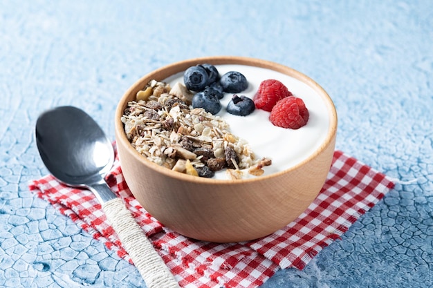 Joghurt mit Beeren und Müsli zum Frühstück in Schüssel auf blauem Hintergrund