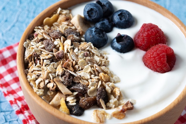 Joghurt mit Beeren und Müsli zum Frühstück in Schüssel auf lbue-Hintergrund