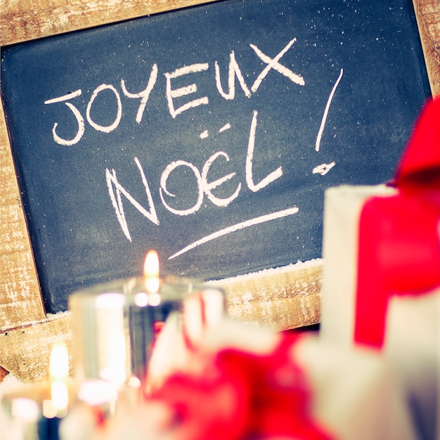 "Joyeux Noel" auf einer Tafel mit Geschenken und Kerze.