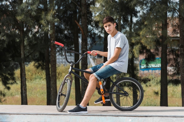 Jugendjunge, der auf Fahrrad am Park sitzt
