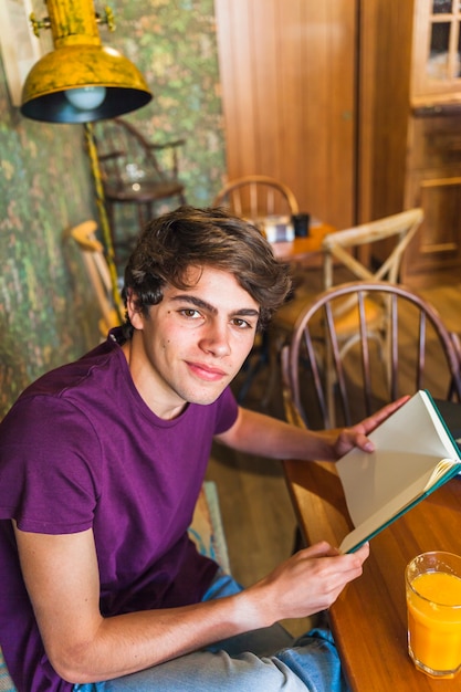 Jugendlich Junge mit dem Buch, das Kamera im Café betrachtet