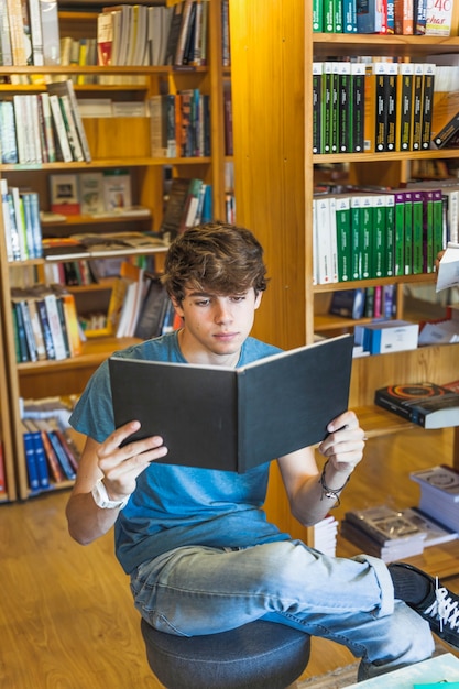 Kostenloses Foto jugendlich jungenlesung auf schemel in der bibliothek