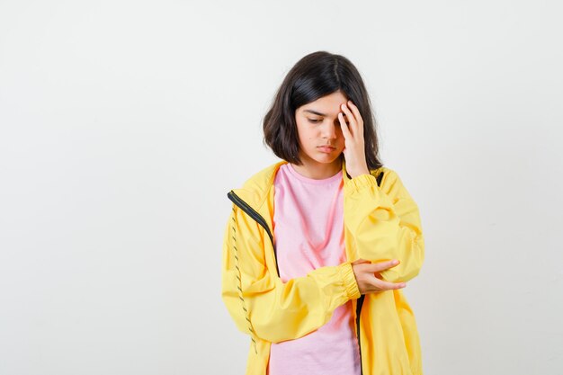 Jugendlich Mädchen, das in denkender Haltung im T-Shirt, in der gelben Jacke steht und verwirrt schaut. Vorderansicht.
