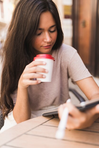 Jugendliche, die MitnehmerKaffeetasse betrachtet digitale Tablette hält