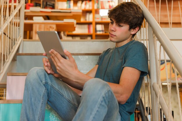 Jugendlicher, der Tablette auf Bibliothekstreppenhaus verwendet