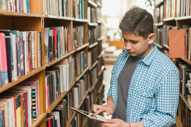 Jugendlicher, der Tablette in der Bibliothek verwendet