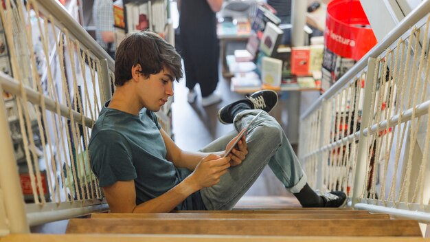 Jugendlicher, der Tablette in der Buchhandlung verwendet