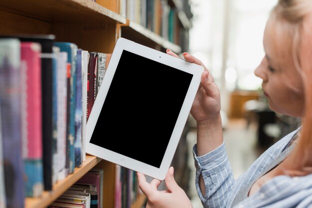 Jugendlicher, der Tablette vom Bücherregal nimmt