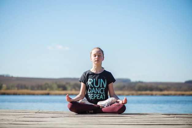 Jugendlicher, der Yoga tut und auf Pier sich entspannt