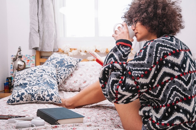 Jugendlicher mit dem Buch, das auf Bett trinkt