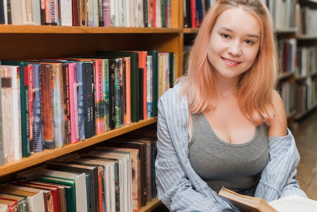 Jugendlicher mit dem Buch, das auf Bücherregal sich lehnt