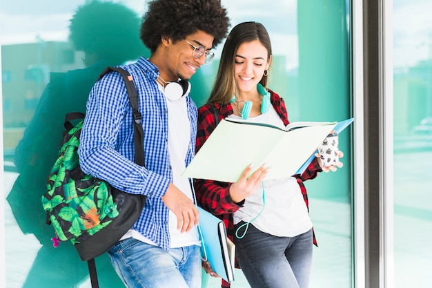 Jugendstudenten mit Büchern und ihren Taschen, die gegen das Glas betrachtet Buch stehen