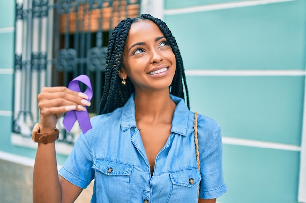 Kostenloses Foto junge afrikanisch-amerikanische frau lächelt glücklich und hält ein lila band, das in der stadt spazieren geht