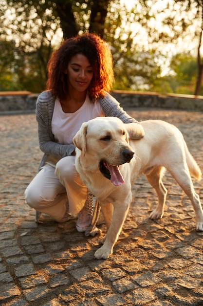 Kostenloses Foto junge afrikanische dame in lässiger kleidung, die hund im park sitzt und umarmt