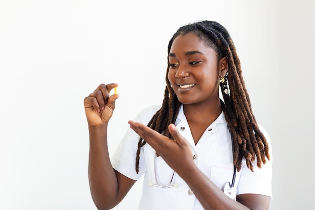 Junge afrikanische Ärztin steht auf grauem Hintergrund und hält revolutionäre Medizin in der Hand