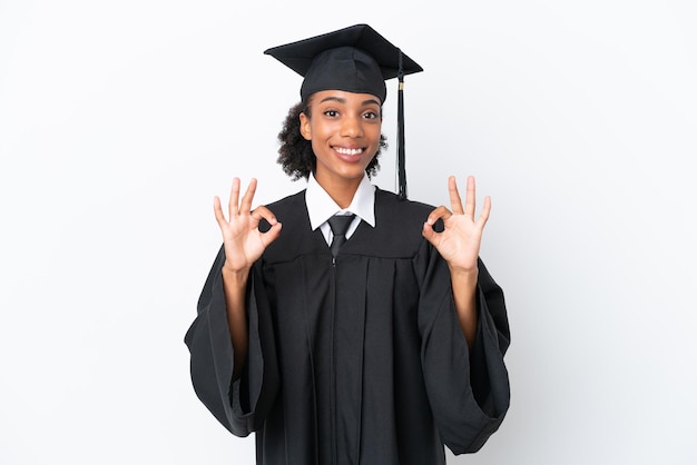 Junge afroamerikanerin mit universitätsabschluss isoliert auf weißem hintergrund, die mit den fingern ein ok-zeichen zeigt