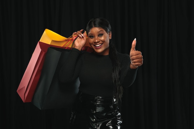 Junge afroamerikanische Frau mit bunten Packungen auf schwarzem Hintergrund einkaufen. Attraktives weibliches Modell.